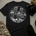 A black short-sleeve t-shirt laid flat on a gray textured surface, featuring a large white circular graphic of two tactical soldiers in gas masks holding rifles. The shirt is styled with camouflage pants, black shoes, and a toy binoculars prop.