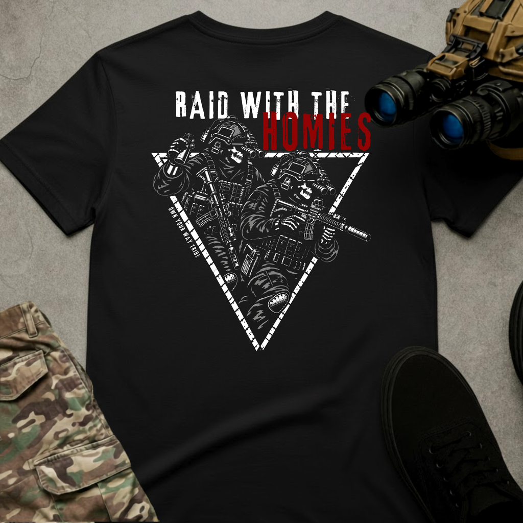 A black short-sleeve graphic T-shirt laid flat on a gray textured surface, surrounded by tactical-style props including camouflage pants, black shoes, and binoculars. The shirt features a large front graphic with the text 'RAID WITH THE HOMIES' in white and red, above a white triangular outline containing illustrated tactical soldiers.